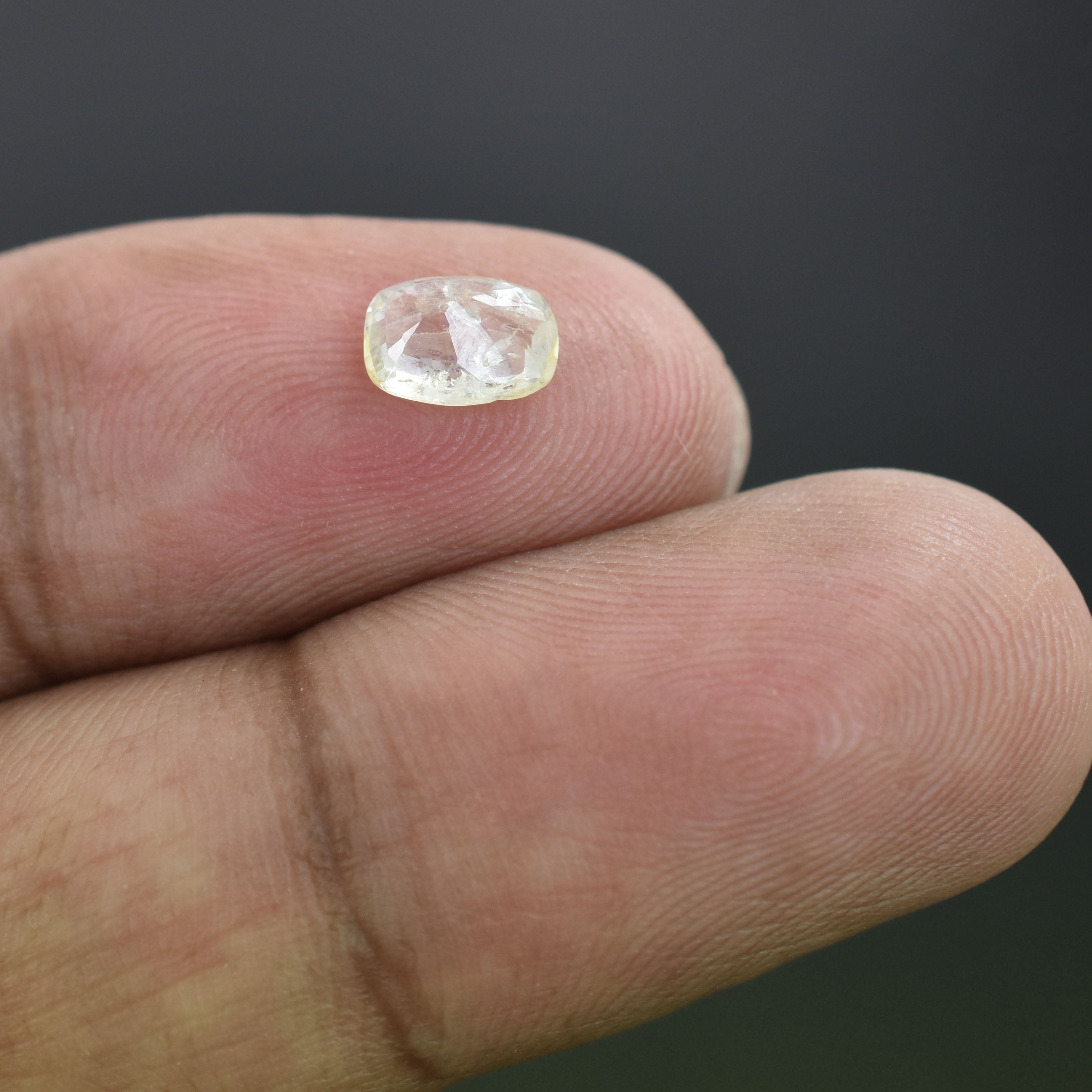 Clear, faceted gemstone held between two fingertips.