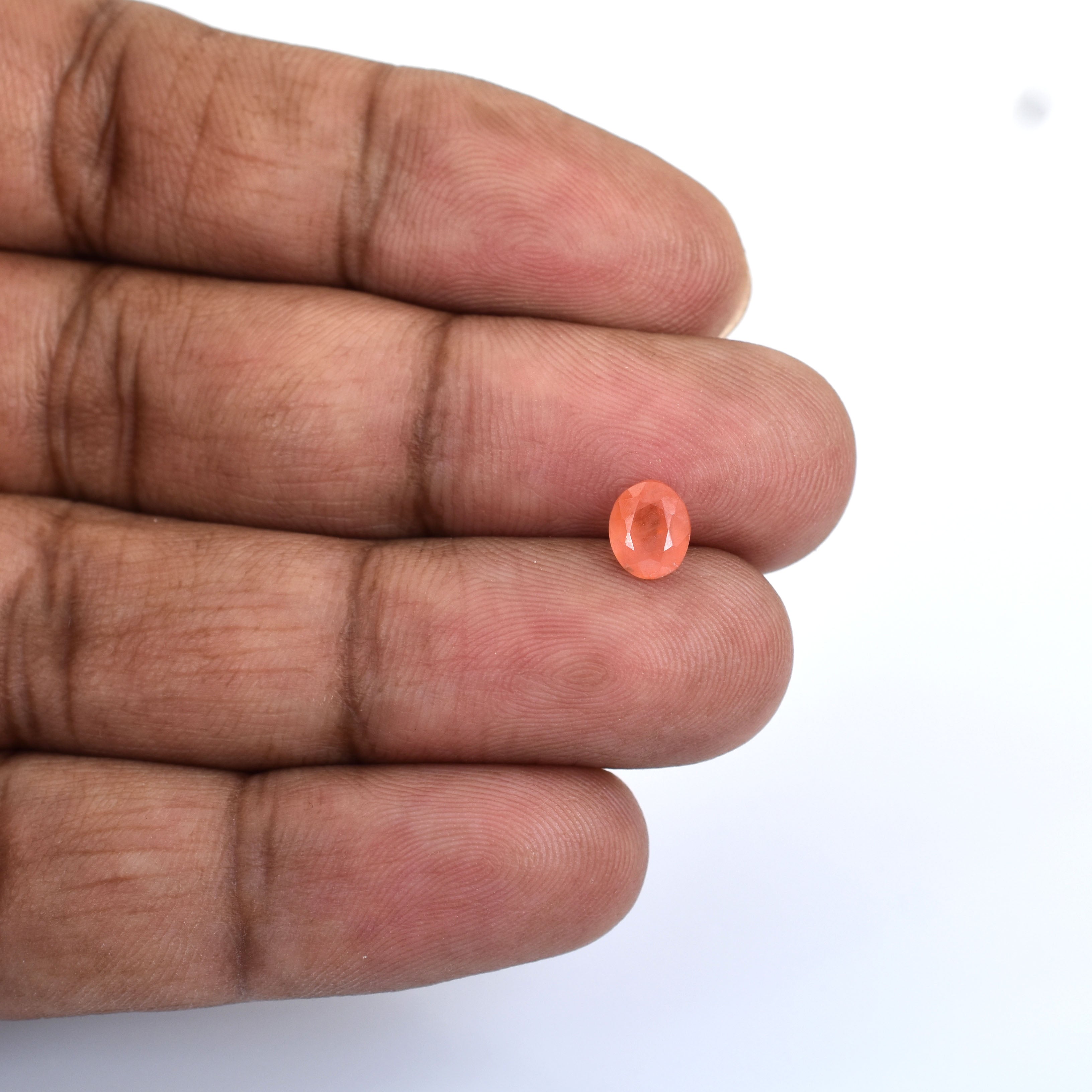 Small, oval-shaped orange gemstone or bead held between fingers.