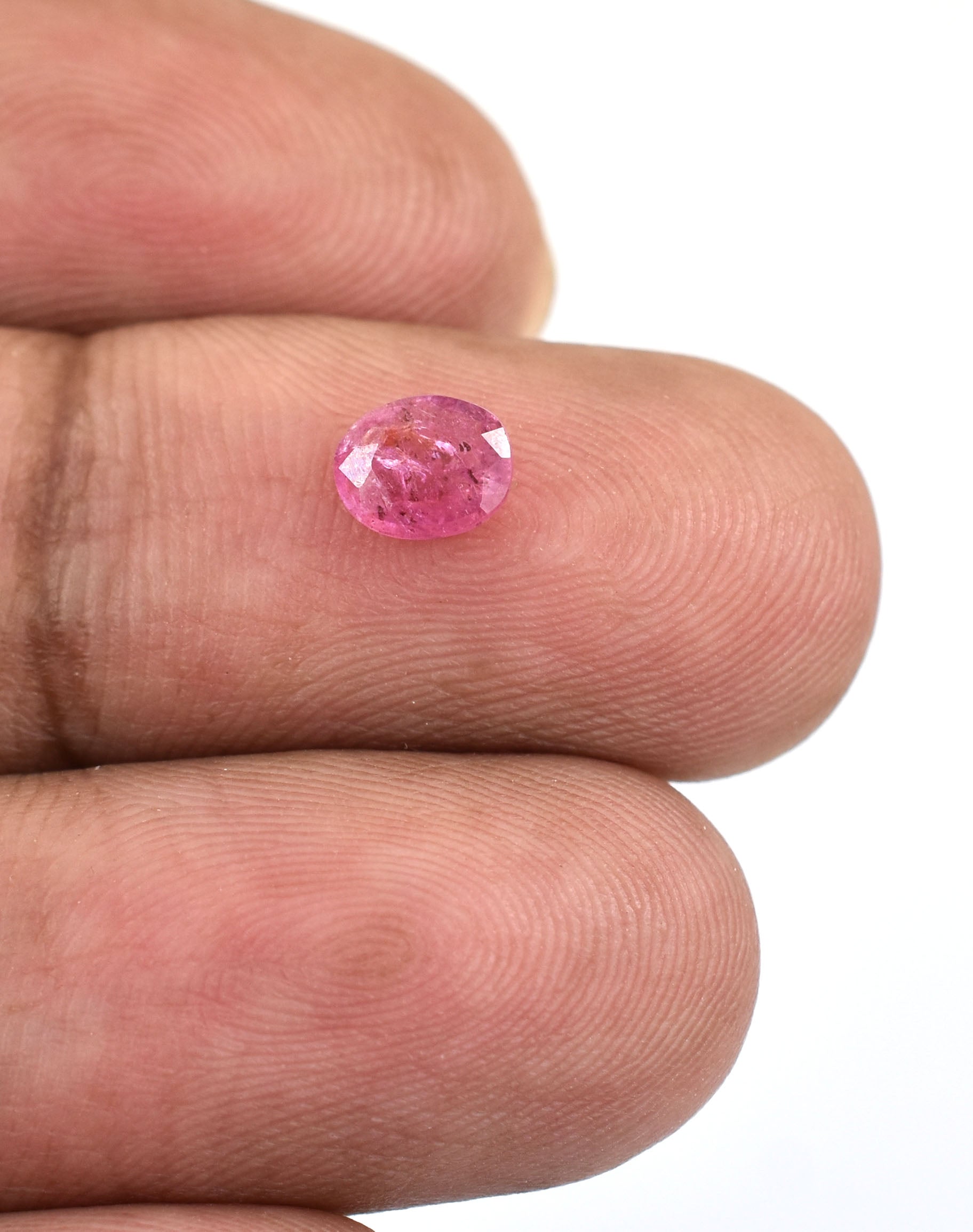 Pink oval-cut gemstone, likely a sapphire or ruby, held between fingers.