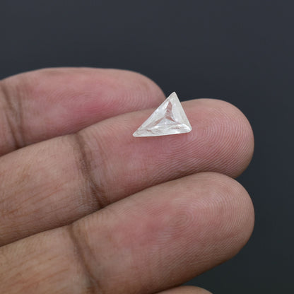 Triangular-cut clear gemstone or diamond held between fingertips.