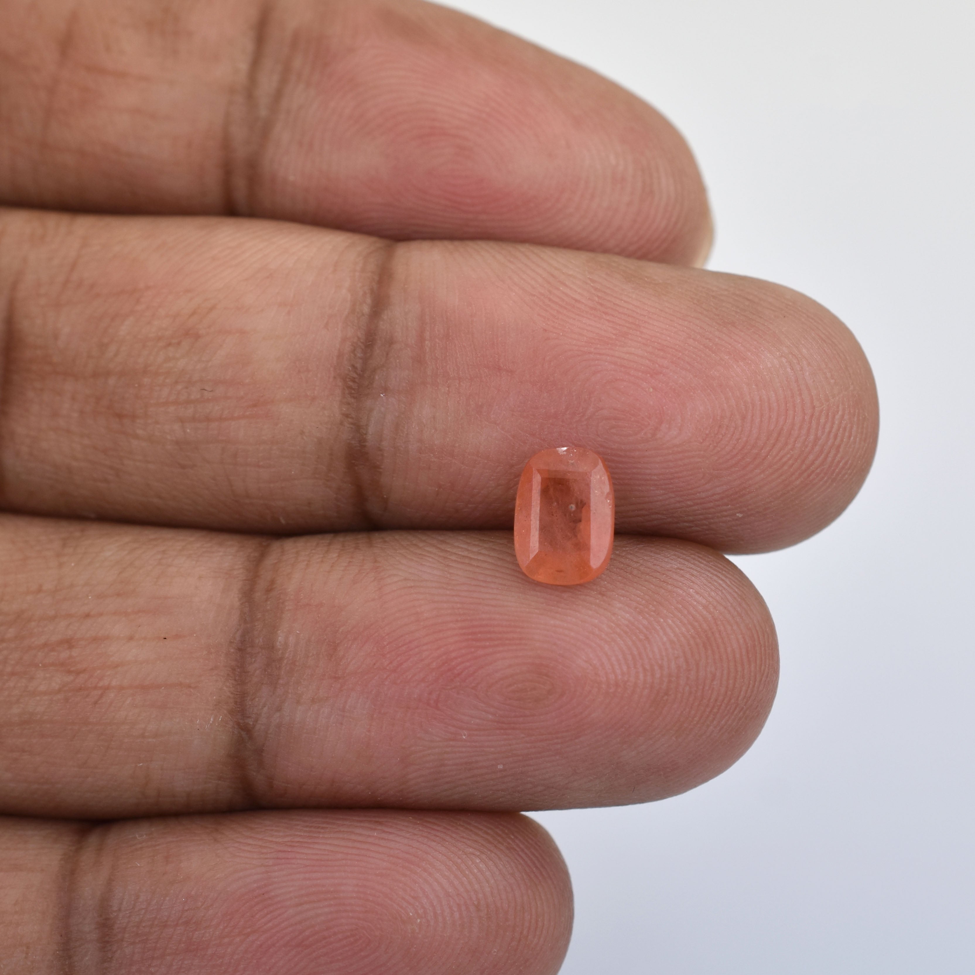 Small, rectangular-cut orange gemstone held between fingers.