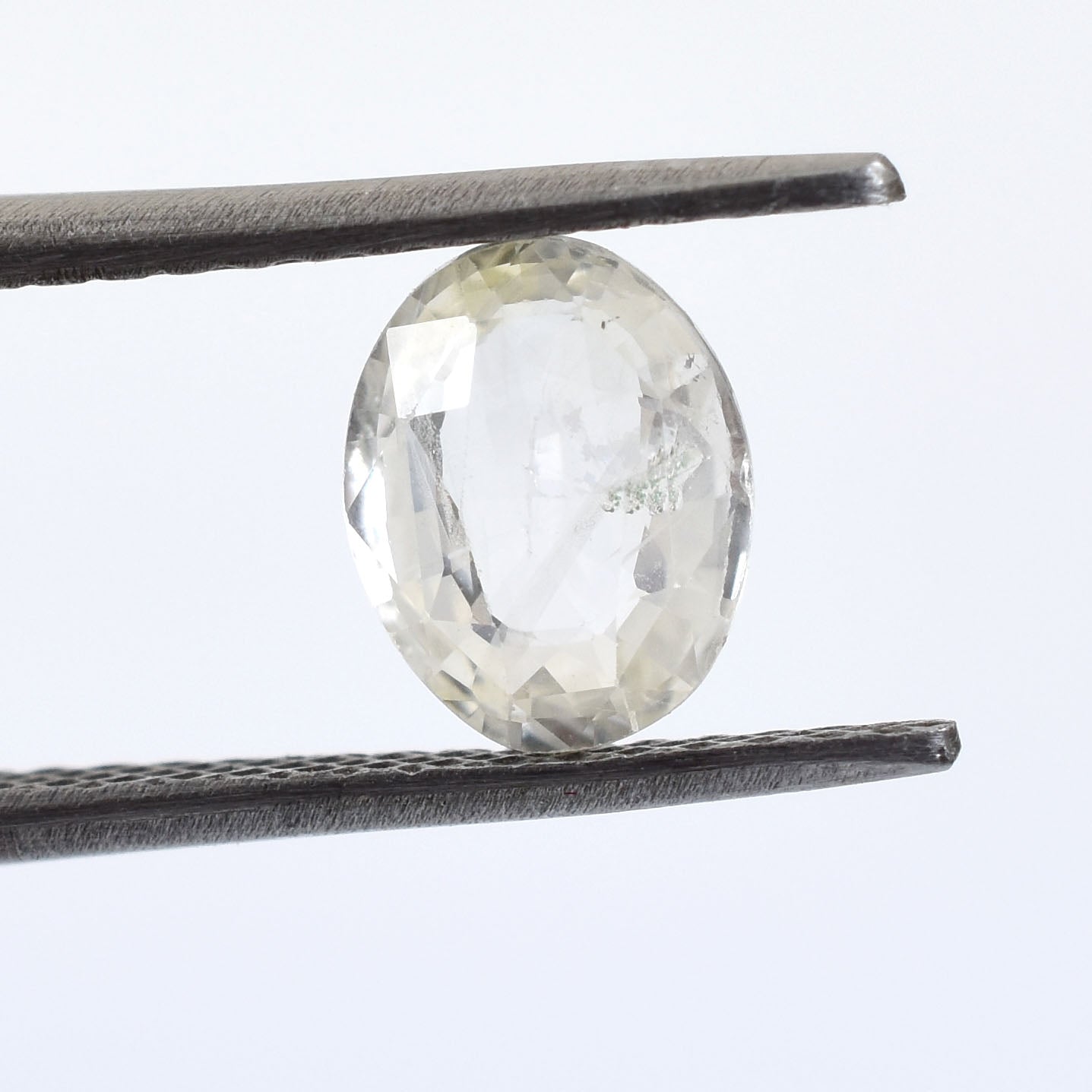 Oval-shaped, faceted gemstone held between tweezers.