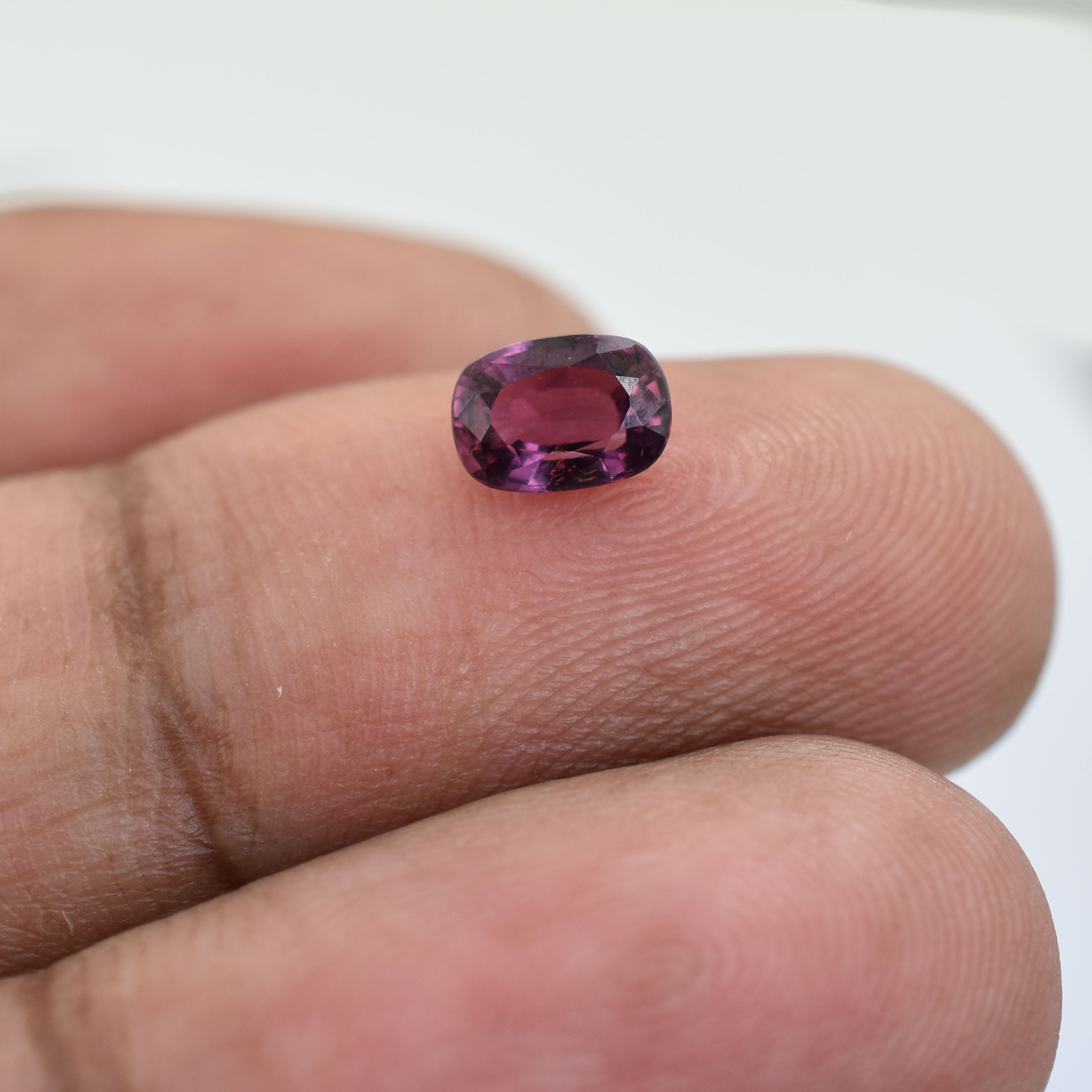 Oval-cut purple gemstone held between two fingers.