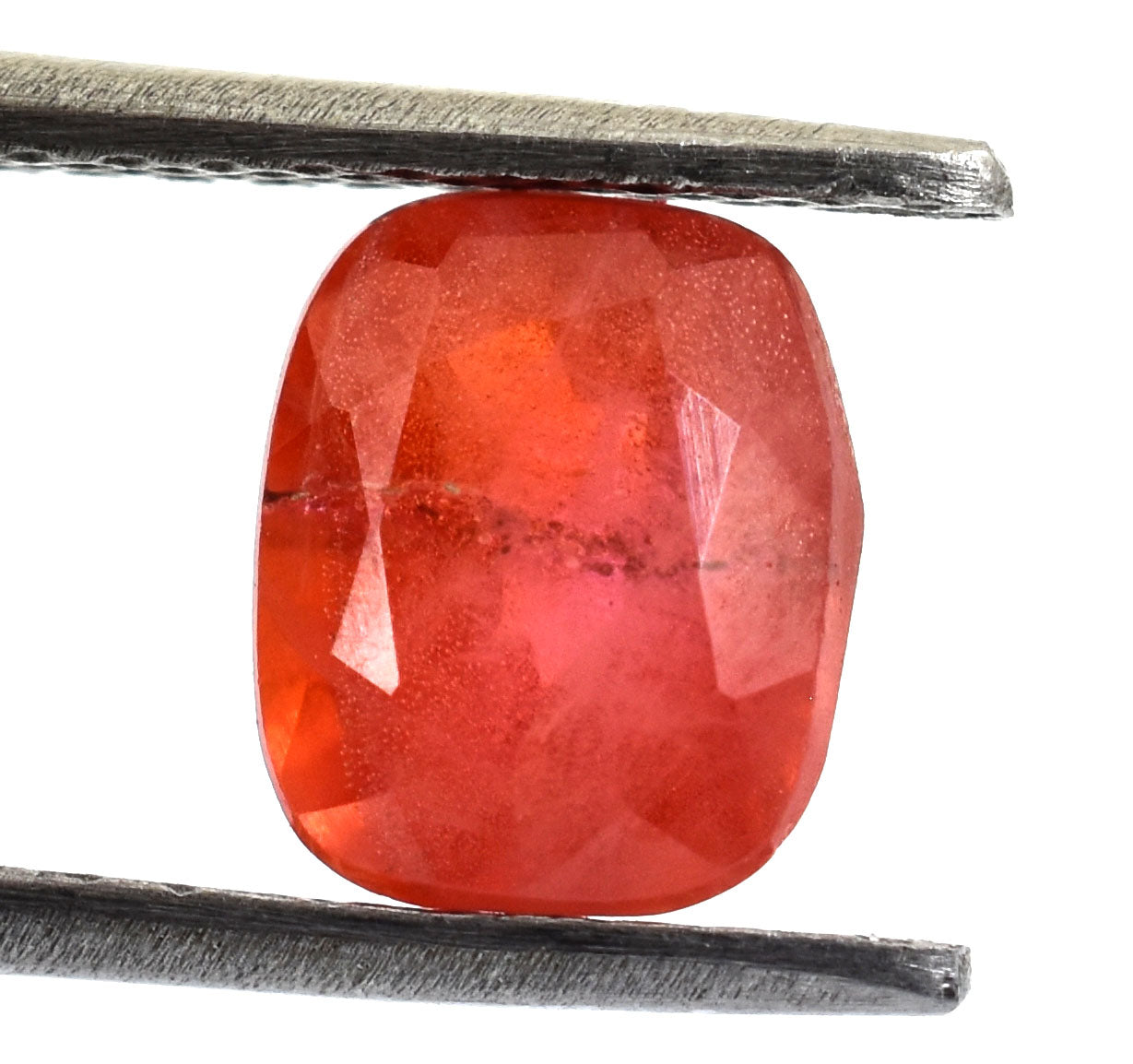 Faceted red gemstone held between metal tweezers or tongs.