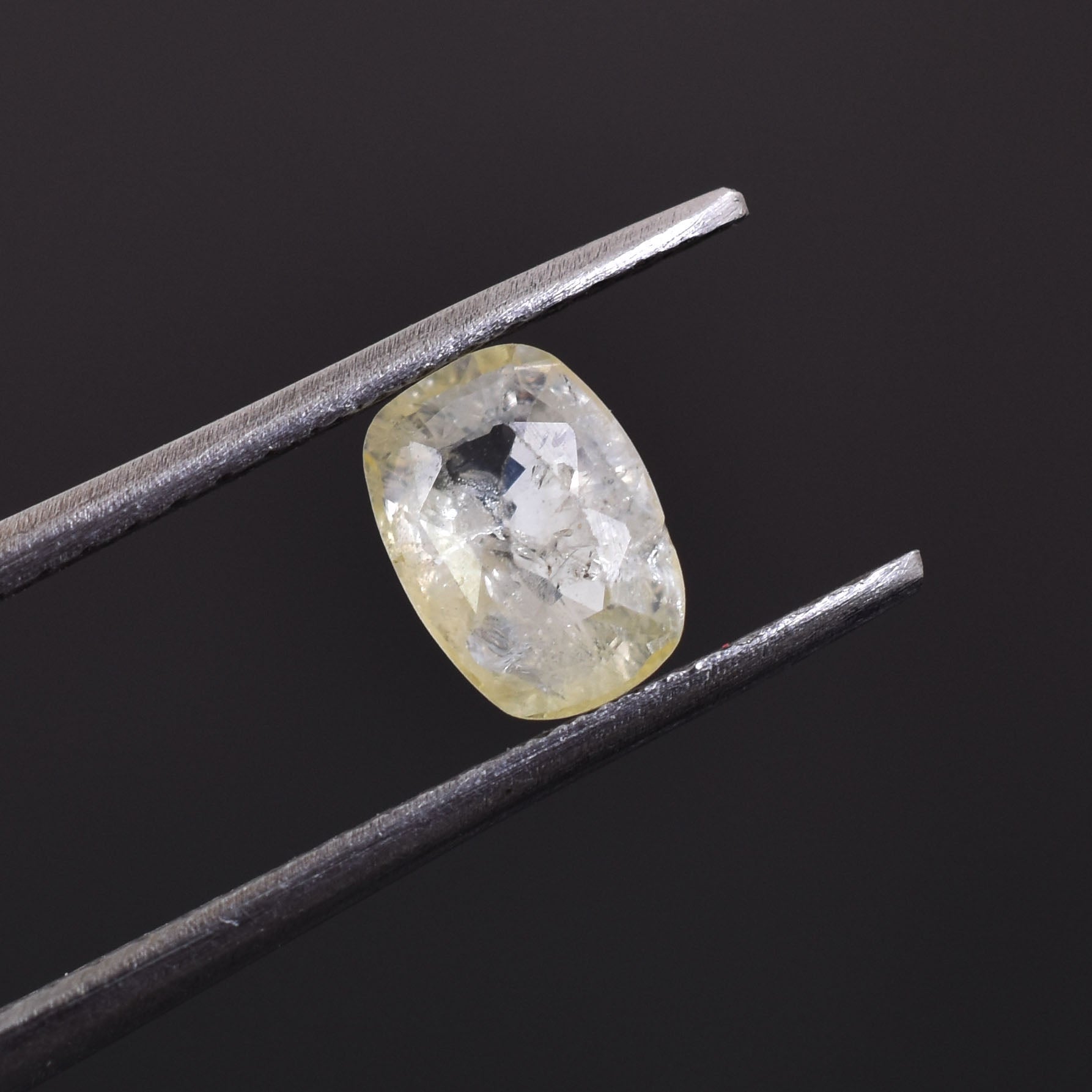 Oval-shaped, translucent gemstone held between metal tweezers.