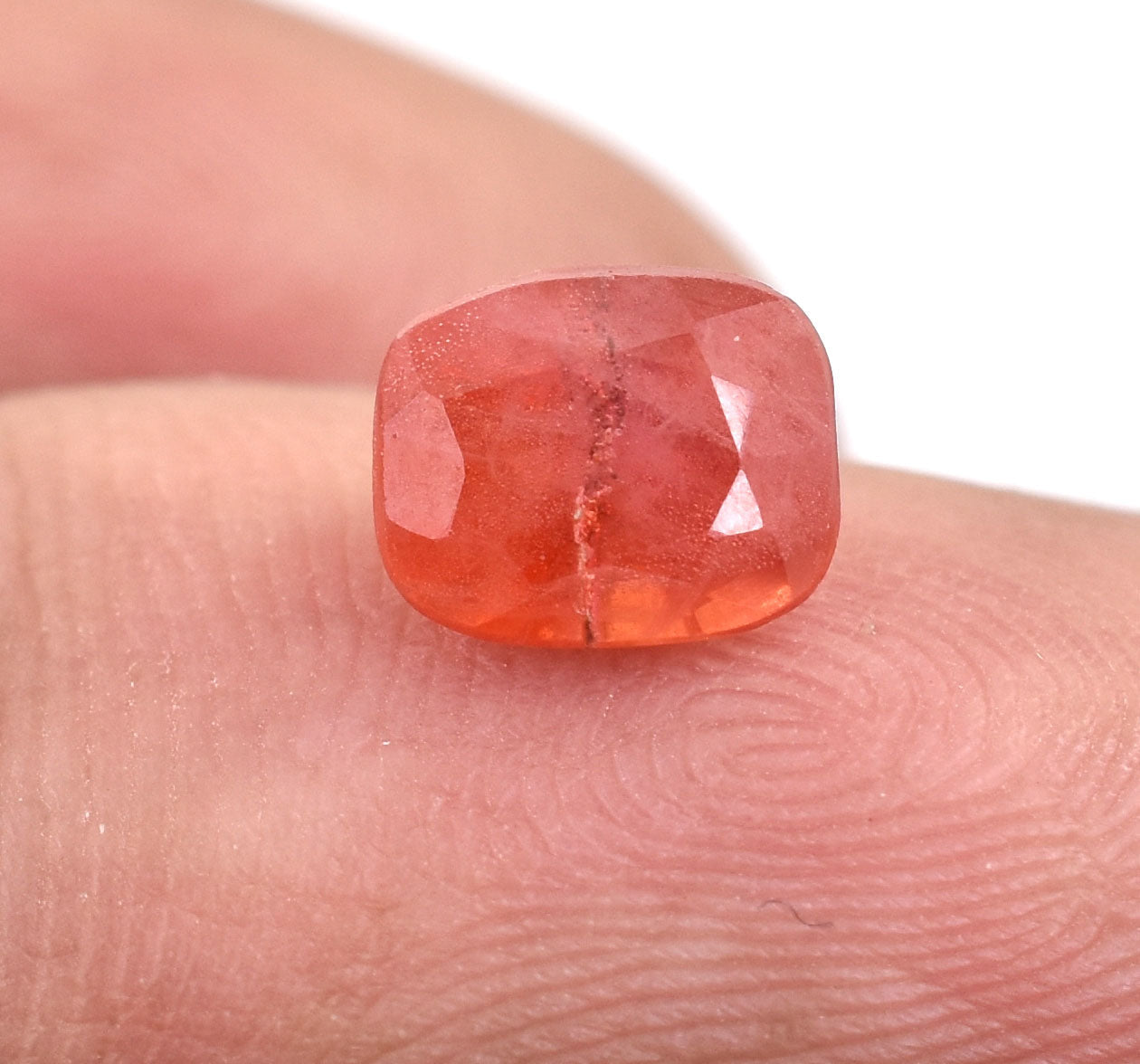 Cushion-cut orange-red gemstone resting on a fingertip.