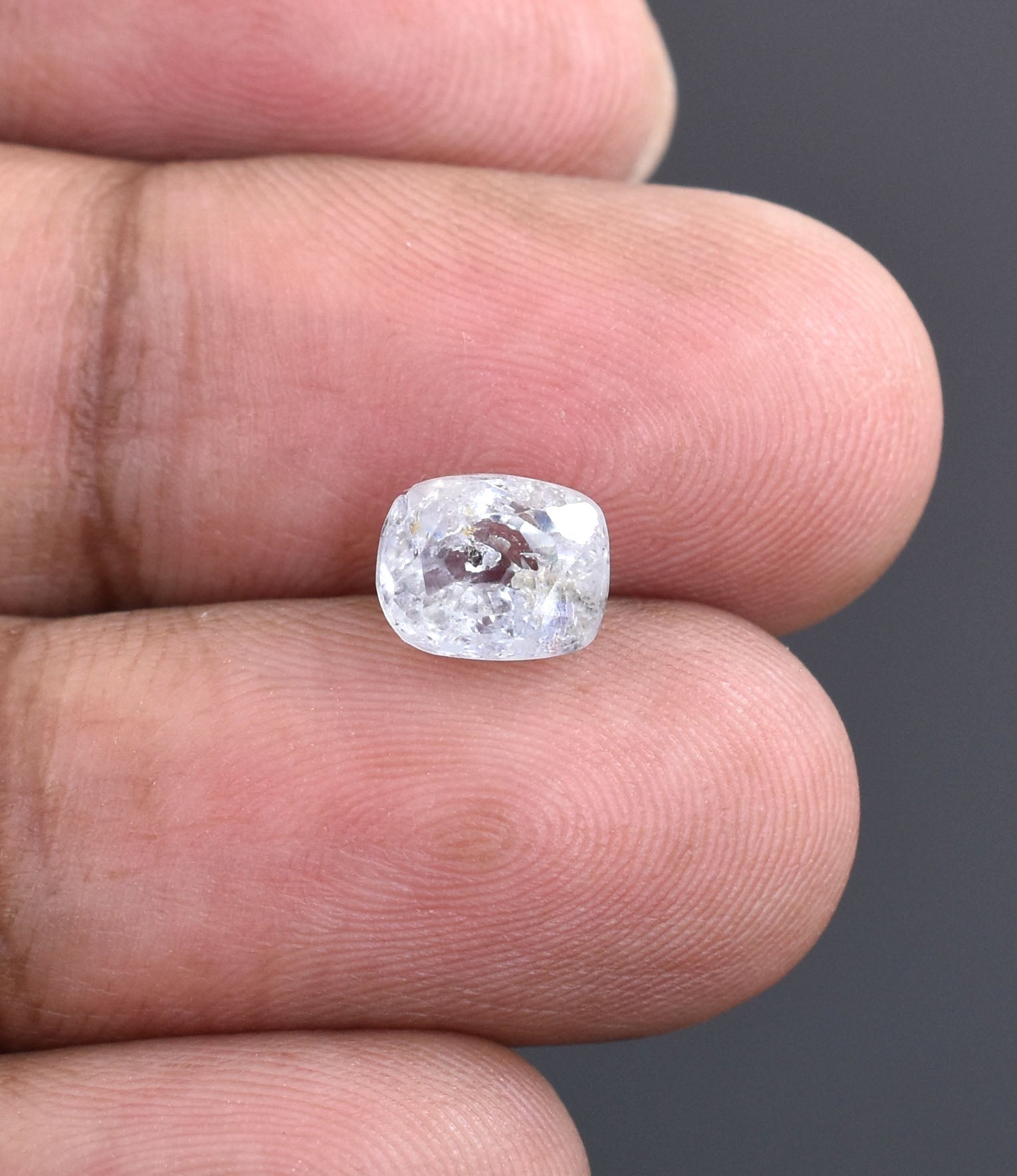 Cushion-cut diamond or gemstone held between two fingers.