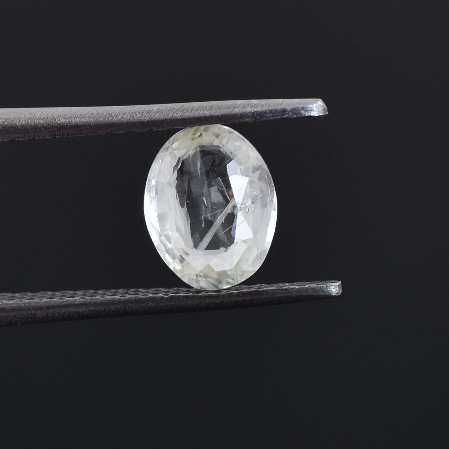 Oval-shaped, transparent gemstone or diamond held by tweezers.