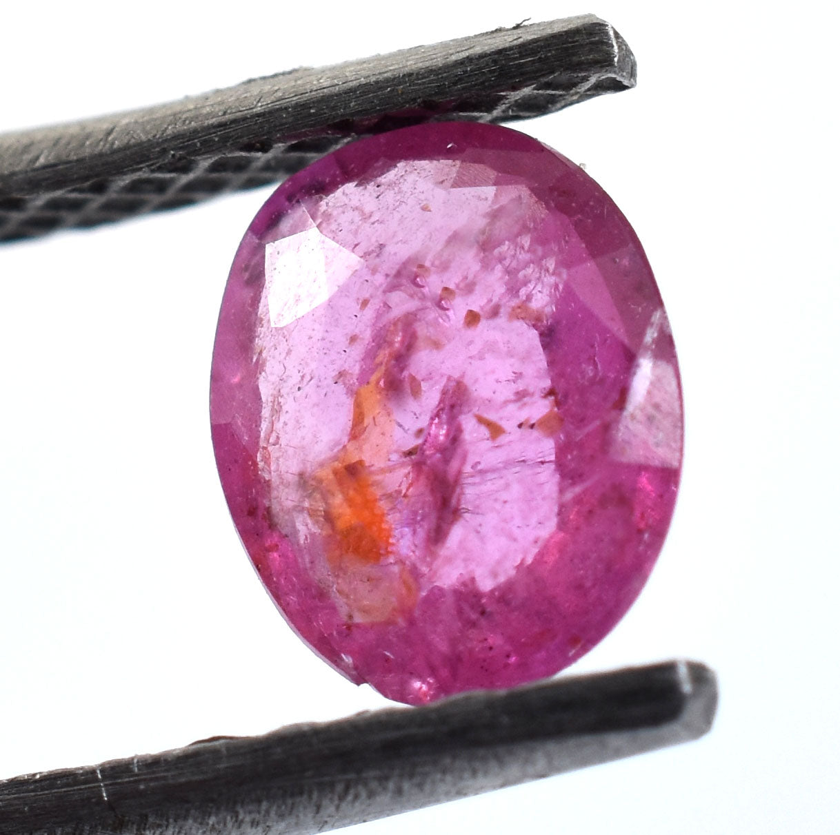 Oval-shaped pink gemstone held between tweezers.